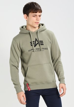 Olivgrüner Hoodie aus weicher Baumwolle mit einer Vordertasche. Verfügt über ein schwarzes Logo und ein rotes Stoffetikett am Saum für Akzente. Verstellbare Kapuze.