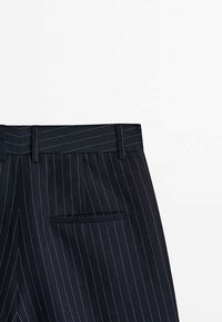 Navy pinstriped trousers made of a textured fabric, featuring a belt looped waistband and a single back pocket.