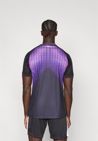 Αθλητική φανέλα σε μαύρο χρώμα με διαβάθμιση που μεταβαίνει σε μοβ. Διαθέτει κοντά μανίκια, ριμπ κολάρο και υφασμένα διακοσμητικά στους ώμους.