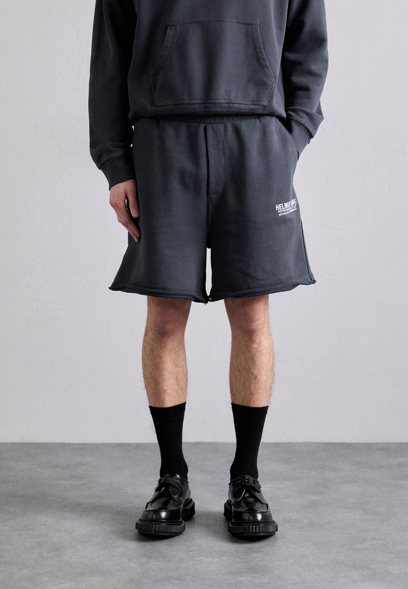 Mørkegrå shorts i bomullsblanding med elastisk midjebånd, med trykk av logo på siden og en avslappet passform, kombinert med svarte sokker og sko.