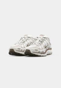 Nike Sneakers mit einem weißen Netz-Obermaterial, beigen Akzenten, strukturiertem Stoff und einer gepolsterten Zwischensohle. Verfügt über ein geschwungenes Design und eine Gummisohle.