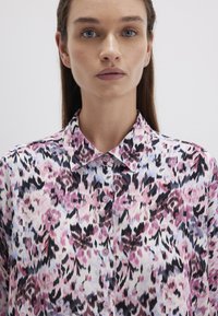 Leichte, knopfbare Bluse mit einem floralem Muster in Pink, Lila und Schwarz auf einem hellen Hintergrund. Glatter Stoff mit klassischem Kragen.