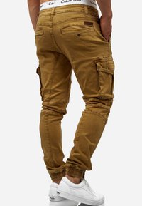Pantalones cargo marrones con puños elásticos, múltiples bolsillos y una cinturilla de Calvin Klein. Tejido texturizado con un diseño ajustado.