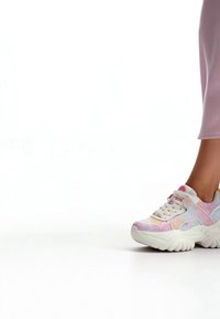 Persona che indossa sneakers chunky rosa pastello e bianche con suole spesse, in piedi su una superficie bianca, con pantaloni rosa.