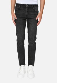 Jeans in denim nero con una vestibilità slim, caratterizzati da cinque tasche, chiusura con bottone e dettagli di cucitura discreti. Abbinati a sneakers bianche.