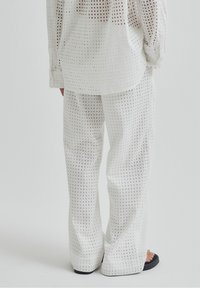 Osoba nosząca luźne białe spodnie i dopasowaną koszulę z długim rękawem w kwadratowy wzór, w połączeniu z czarnymi sandałami na otwartym palcu.