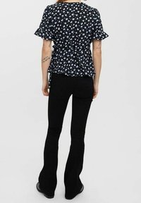 Camicia nera a fiori con maniche corte a volant e un nodo in vita, abbinata a jeans neri a zampa d'elefante e stivali neri.