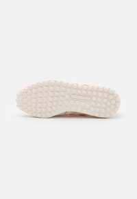 Suola di scarpa con superficie in gomma testurizzata e impugnature tonde, di colore bianco sporco. Il design include tre strisce rosa e blu sui lati.