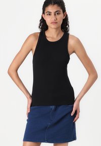 Zwart mouwloos topje van ribbelstof, met een ronde halslijn. Gecombineerd met een blauwe denim rok met zakken en een rechte snit.