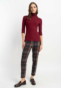 Bordowy golf z rękawami o długości trzech czwartych, w połączeniu z szarymi spodniami w kratkę z czerwonymi akcentami. Dodatkiem do stylizacji są błyszczące, ciemne loafersy.