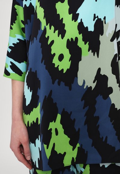 Multicolored blouse featuring large abstract patterns in black, green, blue, and light aqua on a smooth fabric with three-quarter sleeves.