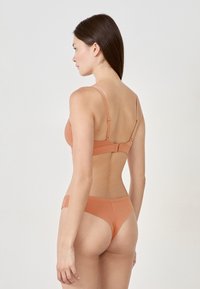 Pomarańczowy komplet biustonosza i stringów, z cienkimi regulowanymi ramiączkami oraz zapięciem z tyłu, wykonany z gładkiego, elastycznego materiału.