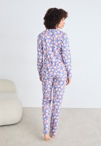 Pajama set s dugim rukavima u ljubičastoj boji s cvjetnim uzorkom u ružičastim i narančastim nijansama. Tkanina izgleda mekano, dizajnirana za udobnost.