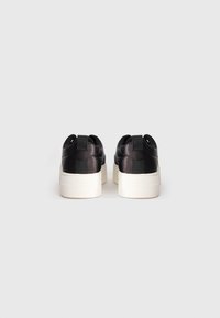 Sneaker in pelle nera con una texture liscia, suole in gomma bianca e linguette sul tallone. Il design presenta una silhouette semplice e moderna.