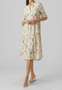 Sukienka w kwiatowy nadruk w kremowym kolorze, z dekoltem w kształcie litery V, krótkimi rękawami i warstwowym, falbaniastym dołem. Wykonana z lekkiego materiału, o zwiewnym kroju.