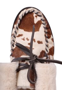 Mocassins à motif marron et beige avec une douce doublure en fourrure, agrémentés de lacets en cuir noir et de coutures décoratives le long du bord.