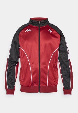 Piros és fekete, cipzáros dzseki fehér részletekkel és oldalzsebekkel, magas nyakkal és bordázott mandzsettákkal. Simább, fényes anyagból készült.