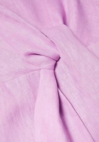 Un tissu en lin rose clair présente un détail noué, affichant une texture douce avec un motif de tissage visible et des variations subtiles de couleur.