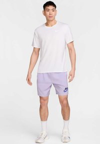 Camiseta blanca de Nike combinada con pantalones cortos lilas claros que presentan un logo azul de "RUN", complementada con zapatillas y calcetines deportivos blancos.