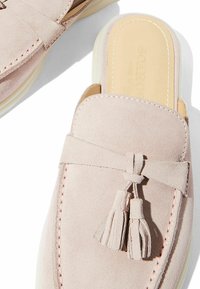 Svijetloružičaste slip-on cipele od antilopa imaju zaobljeni vrh, dekorativne rese i kontrastnu bijelu gumenu podlogu s prošivenim detaljima.