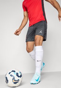 Punane spordijakk mustade aktsentidega, hallid lühikesed püksid vertikaalsete triipudega ja logoga, valged sokid ning helesinised jalgpallikingad, mis on mustrilise jalgpalliga kõrvuti.