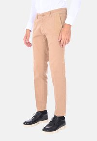 Pantaloni di cotone beige con una vestibilità dritta, dotati di tasche frontali e una texture liscia. Abbinati a scarpe nere e una camicia bianca.
