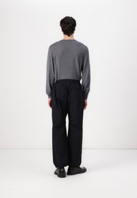 Chemise grise à manches longues avec une coupe décontractée et un col arrondi, assortie à un pantalon noir ample et des chaussures noires.