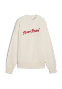 Krēmskrāsas sporta krekls ar ribotiem piedurknēm un apakšmalu, uz kura priekšpuses ir sarkanie izšuvumi ar tekstu "Puma Resort" un mazais logo.