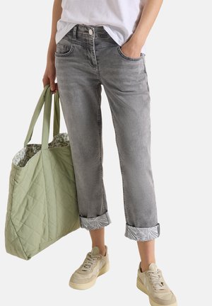 Person iført opsmøgede grå jeans, off-white sneakers, hvid skjorte, som holder en stor quiltet lysegrøn tote taske med mønstret for.
