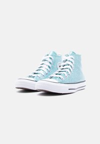 Ζευγάρι sneakers ψηλού στελέχους σε λαμπερό ανοιχτό μπλε χρώμα με λευκά κορδόνια και λαστιχένιες σόλες, τοποθετημένα σε ελαφρώς διαγώνια θέση προς τα αριστερά σε λευκό φόντο.