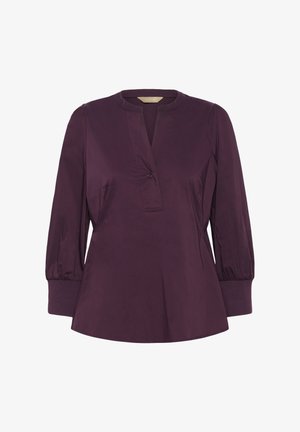 Lila hosszú ujjú blúz kerek nyakkal, gombos díszítéssel elöl és gumírozott mandzsettákkal. Sima anyag, enyhén bővülő fazonban.