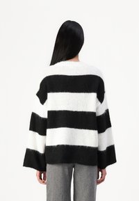 Black and white striped sweater with a relaxed fit, wide sleeves, and a soft, textured knit. Worn over gray tailored pants.