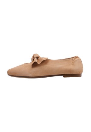 Chaussure plate en suede beige avec un bout arrondi, un nœud décoratif à l'avant, une ouverture élastiquée et une semelle basse marron. Texture lisse sur l'ensemble.
