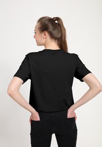 Czarny bawełniany t-shirt z krótkimi rękawami, luźnym krojem, okrągłym dekoltem i gładką fakturą. Noszony z ciemnymi dżinsami, ręce w kieszeniach.