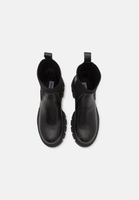 Bottes à cheville en cuir noir avec semelles épaisses et cols élastiques en tricot côtelé, vues de dessus sur un fond blanc.