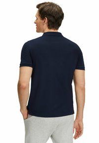 Granatowa koszulka polo z krótkim rękawem. Miękka tkanina, klasyczny kołnierzyk i proste wykończenie. Noszona z jasnoszarymi spodniami dresowymi.