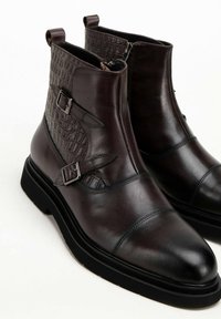 Botines de cuero marrón oscuro que presentan un panel de textura con patrón de cocodrilo, doble hebilla lateral y una suela de goma gruesa para mayor estabilidad.