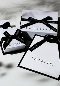 Tre presentlådor i vitt med svart band, pryds av logotypen "LATELITA" i modern stil på framsidan. Många olika storlekar är staplade tillsammans.