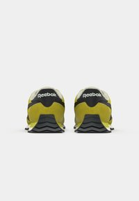 Par žutih i crnih Reebok tenisica prikazanih s leđa, s teksturiranim potplatima i bijelim logotipom brenda na stražnjim trakama.
