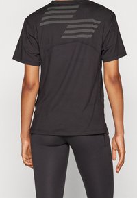 Camiseta atlética negra con diseño perforado en la parte posterior, de mangas cortas y fabricada con un tejido ligero. Se ajusta estrechamente al cuerpo.