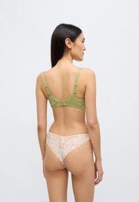 Πράσινο δαντελένιο σουτιέν με ρυθμιζόμενους ιμάντες και κούμπωμα με αγκράφα, συνδυασμένο με ροζ δαντελένιο στρινγκ με λουλουδάτα σχέδια και κυματιστό τελείωμα.