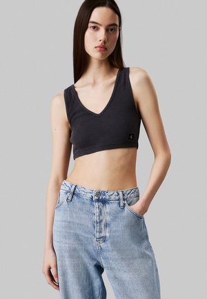 Zwart geribbeld crop top met een V-hals, gecombineerd met lichtblauwe high-waisted jeans met een vervaagd textuur en zijzakken.