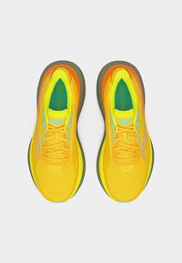 Φωτεινά κίτρινα αθλητικά παπούτσια με πορτοκαλί λεπτομέρειες, μπλε λογότυπα, πράσινες εσώσολες με την ένδειξη "FORMFIT" και γκρι εξωτερικές σόλες, απεικονιζόμενα από πάνω.