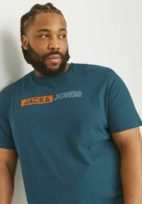 Teal kortærmet T-shirt lavet af blødt stof, med "JACK&JONES" logoet i orange og grå placeret på brystet.