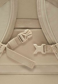 Beige rygsæksektion med struktureret mesh-stof, justerbar rem med plastikspænde, og et fremtrædende Nike-logo.