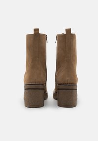 Bottines en daim marron avec un talon large, dotées d'une fermeture éclair latérale et de détails de couture. Texture lisse et accents de design minimalistes.