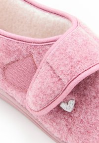 Pantofole di feltro rosa con una consistenza morbida, caratterizzate da un dettaglio ricamato a forma di cuore e una fascia con chiusura a strappo per una vestibilità regolabile.