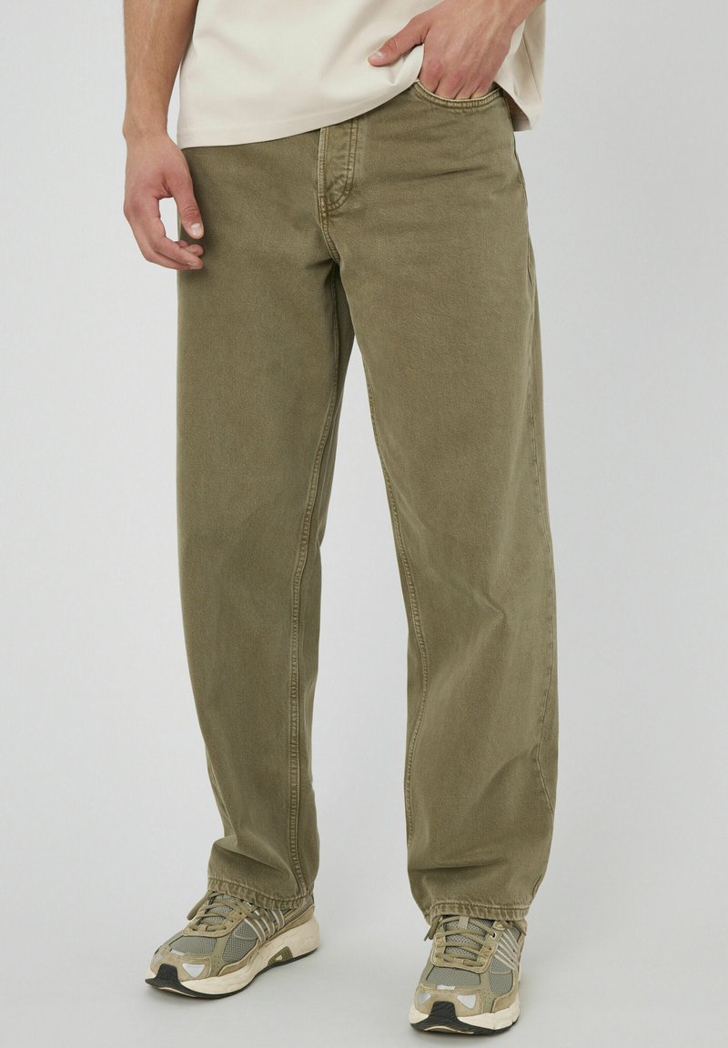 Pantalons en coton vert olive avec une coupe droite, dotés de poches avant et d'une taille visible, associés à des baskets grises et beiges.