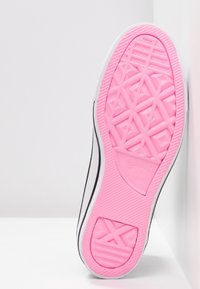 Semelle en caoutchouc rose avec motif géométrique, dessus en toile noire et blanche, présentant un bord blanc et un logo embossé sur la semelle.