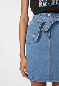 Světle modrá džínová sukně s pasem na pásek, poutek na pásek a šikmou přední kapsou. Vyznačuje se hladkou texturou a jemnými švy.